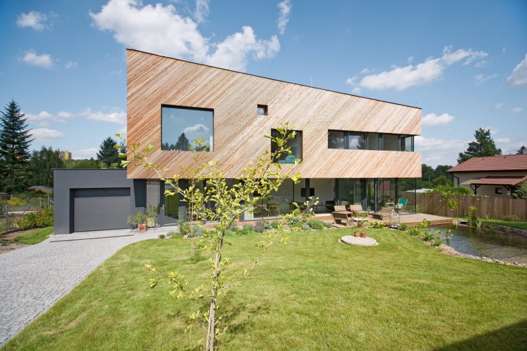 Architektonické řešení navazuje na zahrádkářskou minulost parcely a koncept projektu řadových domů. Protáhlá obdélníková stavba má plně prosklené přízemí, na…