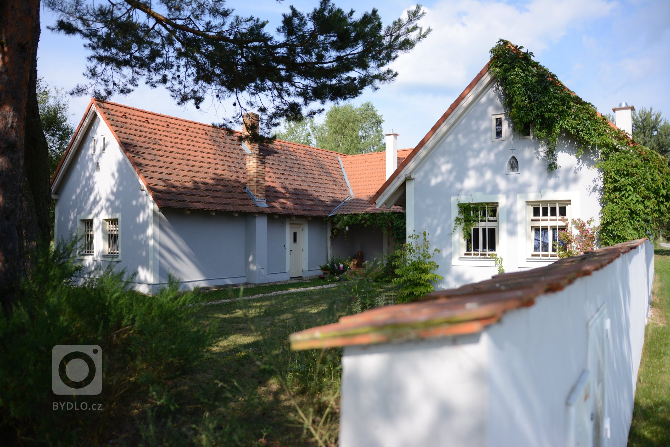 Klasické jihočeské stavení ve tvaru U s šedo-bílou omítkou a klasickými okny.