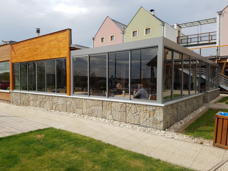 Hliníkovú pergolu jsme osvětlili a zavedli do ní všechny inženýrské sítě, díky čemuž se stala plnohodnotnou venkovní restaurací a barem.&nbsp;Boční zakrytí…