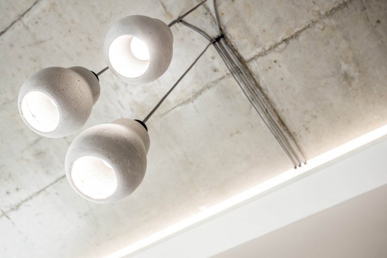 Na betonovém stropě jsou světla vedeny přiznanou kabeláží... design je třeba držet, takže jsme zopakovali materiál stropu i na svítidlech.